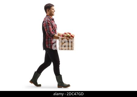 Full length profile shot of a young man walking and carrying a crate with apples isolated on white background Stock Photo