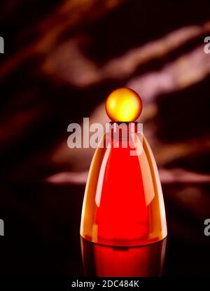 Fragrance bottle in moody, dark, surreal environment.  Reflections on the shiny exterior, glowing yellow circle for the top, with red saturated base Stock Photo