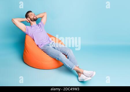Full length body size photo of bearded freelancer chilling relaxing laying in orange beanbag isolated on bright blue color background Stock Photo
