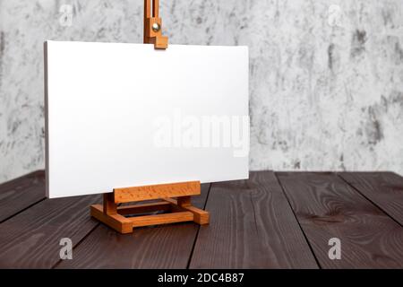 White blank canvas stretched on subframe and an easel standing on a brown wooden table. Mockup Stock Photo