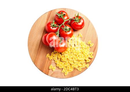 Heap farfalle italian pasta and Fresh Red ripe tomatoes on a green branch laying on wooden beech board. Isolated on white background Stock Photo