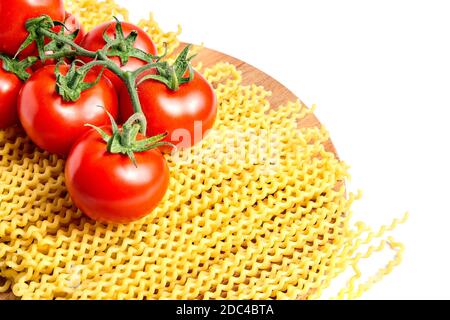 Heap fusilli bucati lunghi italian pasta and Fresh Red ripe tomatoes on a green branch laying on wooden beech board. Isolated on white background Stock Photo