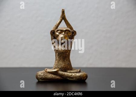 A gold colored meditating monkey statue sitting on a black surface, the background of the picture is white and blurry. Stock Photo