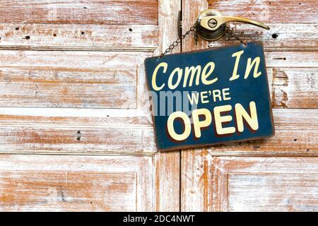 Come In We're Open on the wooden door, copyspace on the left. Stock Photo