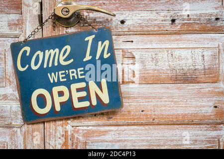 Come In We're Open on the wooden door, copyspace on the right. Stock Photo