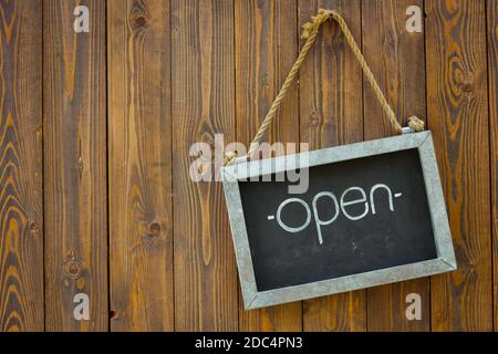 blackboard with the word open with rope on wooden door of a coffee shop. Copyspace on the left. Stock Photo