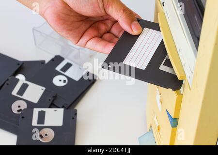 Hand inserting a 3.5-inch floppy disk into a floppy drive slot on a desktop computer. Selective focus. Stock Photo