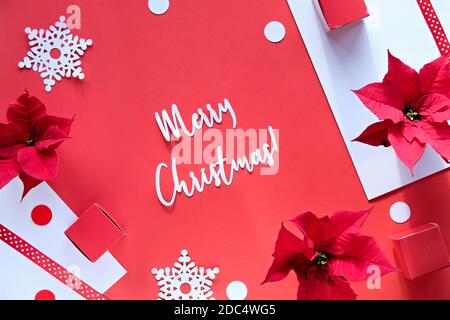 Text Merry Christmas. Poinsettia, snowflakes, red white paper confetti. Top view, monochrome design Stock Photo