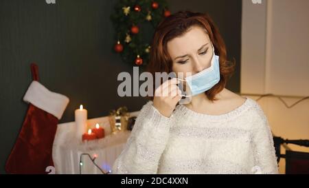 Cute young woman puts on medical mask feeling down with gift box in hands Stock Photo
