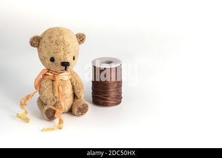 A small vintage handmade bear sits on a spool of thread on a white background. Hobby, needlework. Handmade gifts for any occasion. Copy space. Stock Photo