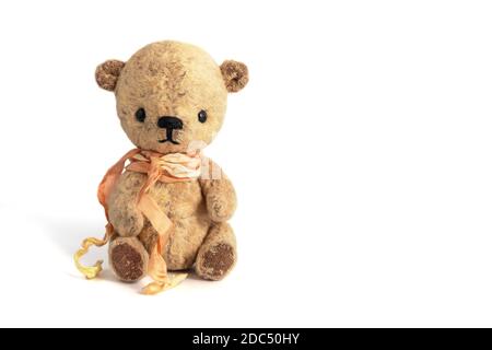 Vintage handmade teddy bear with a ribbon around the neck sits on a white background. Gift or surprise for an important holiday. Close-up. Copy space. Stock Photo