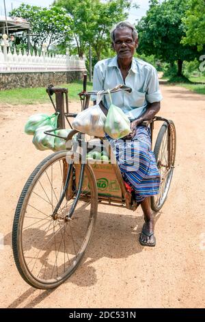 A physically challenged man riding a modified bicycle on his way home after buying fruit at a local market at Sigiriya in central Sri Lanka. Stock Photo