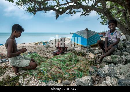 Boys repair a fishing net under the shade of a tree on Delft Island in the northern Jaffna region of Sri Lanka Stock Photo