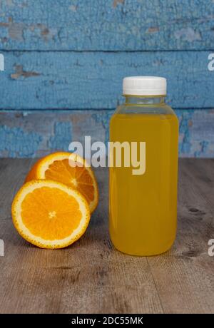plastic bottle with fresh juice and sliced orange. yellow drink on a wooden background. wooden boards with scuffed blue paint. Stock Photo