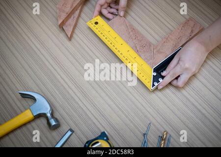 Female hands using a try square to check that the woodworking corners are square with a set collection of working hand tools for the wooden, Toolset w Stock Photo