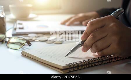 Business people keep notes of income and expenses in a money-saving idea notebook for the future. Stock Photo