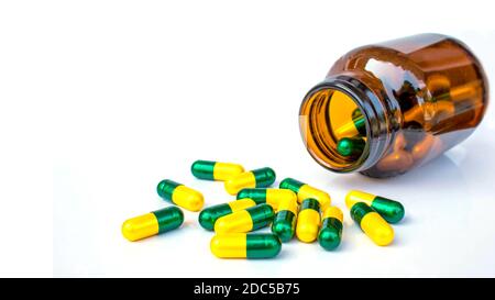 Many yellow-green capsules are pouring out of the bottle. Isolated on white background. Stock Photo