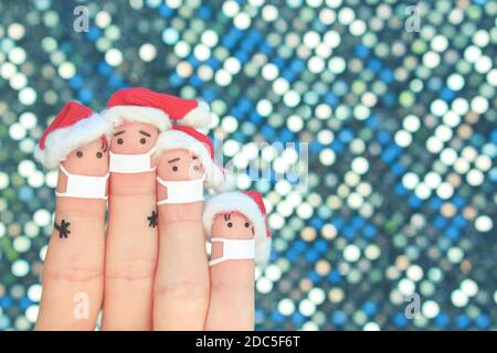 Fingers art of family in medical mask from COVID-2019 celebrates Christmas. Concept of people in New Year hats. Stock Photo
