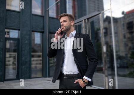 Young man in a black suit talking on the phone and looking serious Stock Photo