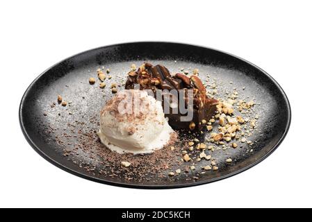 Chocolate brownie with vanilla Ice сream on black plate garnished with nuts and flower. Isolated on white background Stock Photo