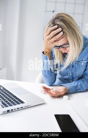 Pretty young woman taking painkillers while sitting in office Stock Photo