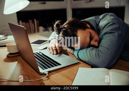 Tired caucasian businessman sleeping at office desk after a long night shift of work, working in apartment  Stock Photo