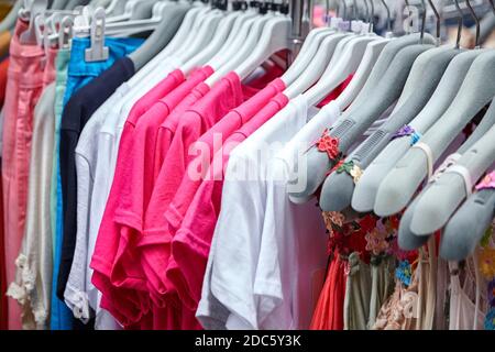Colorful women's summer dresses and t-shirts on hangers in a retail shop. Fashion and shopping concept Stock Photo