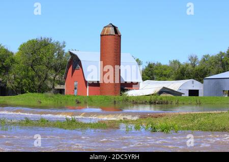 Kansas Red Barn and Silo with flood water in the spring in Hutchinson Kansas USA out in the country. Stock Photo