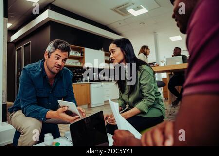 Mixed group of colleagues gathered to discuss new project in office working on laptops and paper work  Stock Photo