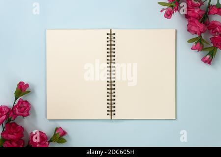 Top Table Spiral Notebook or Spring Notebook Mockup in Unlined Type on Center Frame and Rose Flowers at Bottom Left and Top Right Corner on Blue Paste Stock Photo