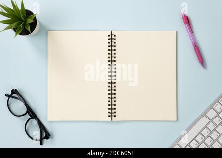 Top Table Spiral Notebook or Spring Notebook Mockup in Unlined Type on Center Frame and Red Pen and Glasses and Office Plant and Keyboard on Blue Past Stock Photo