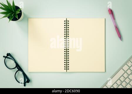 Top Table Spiral Notebook or Spring Notebook Mockup in Unlined Type on Center Frame and Red Pen and Glasses and Office Plant and Keyboard on Blue Past Stock Photo