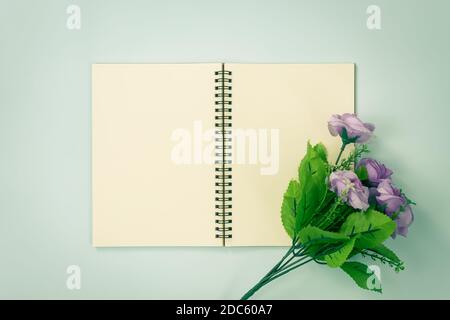 Top Table Spiral Notebook or Spring Notebook Mockup in Unlined Type on Center Frame and Purple Flowers at Bottom Right Corner on Blue Pastel Minimalis Stock Photo