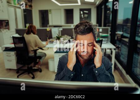 Stressed caucasian businessman holding his temples anxious about meeting deadlines working late hours in office  Stock Photo