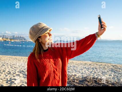 Beautiful young caucasian woman solo traveller make a self portrait herself on the beach at sunset or dawn - Alone female person smiling looking at th Stock Photo