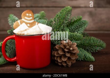 Cocoa hot chocolate in red mug with marshmallows and gingerbread cookie man , fir tree branches and pine cones on dark wooden background Stock Photo