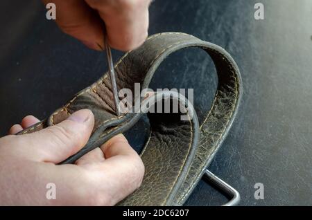 A man makes holes in a leather collar with an awl. Hands of an adult man with a metal awl and a wide collar. Pet equipment repair. Selective focus. Stock Photo
