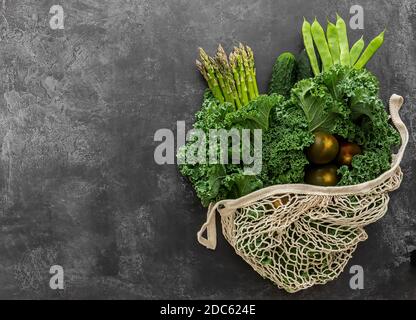 Green vegetables in the string bag. Asparagus, broccolini, kale, cucumber, and tomatoes. No plastic shopping concept. Stock Photo