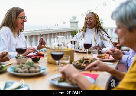 Happy multiracial senior friends having fun dining together on house patio - Elderly lifestyle people and food concept Stock Photo