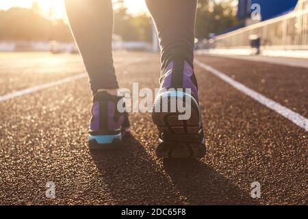 Runner feet running on stadium tracks closeup on shoe. Woman fitness sunset jog workout welness concept. Sunshine on background. Stock Photo