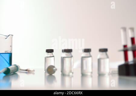 Vaccine vial research concept on white bench with chemical glassware in laboratory . Front view. Horizontal composition. Stock Photo