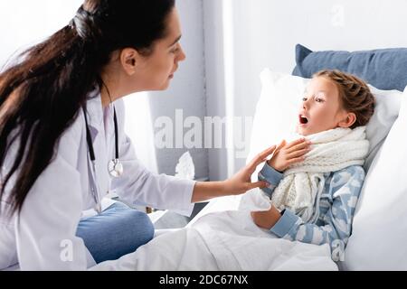 pediatrician examining sore throat of diseased girl lying in bed Stock Photo