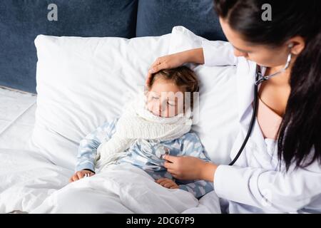 high angle view of pediatrician touching head of sick girl and examining her with stethoscope on blurred foreground Stock Photo