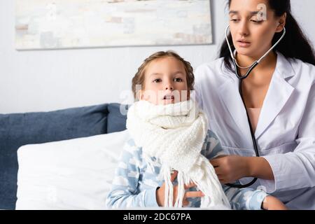 pediatrician examining girl, wrapped in warm scarf, with stethoscope Stock Photo