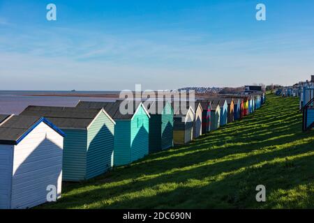 Rows of colourful beachuts cast strong shadows of hut shapes on the huts in front on the shore of the Thames Estuary, Tankerton, Whitstable, Kent, UK Stock Photo