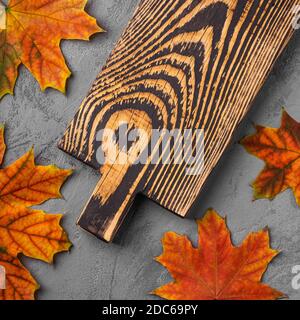 Handcrafted old wooden cutting board with autumn leaves on concrete background, top view Stock Photo