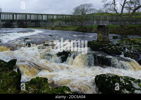 Rocky white water rapids with a wooden footbridge over it, Linton Falls, Nidderdale, North Yorkshire, England, UK. Stock Photo