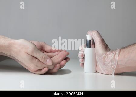A pair of hands wait to be disinfected by a hydroalcoholic gel pressed by a hand protected with semi-transparent gloves on white background. Stock Photo
