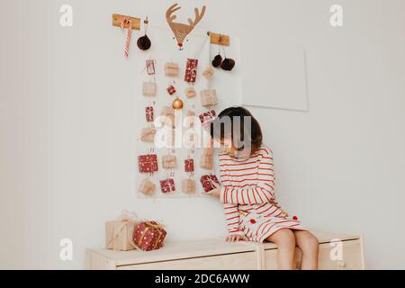 Cute girl opening Christmas Advent calendar gifts. Wrapped gifts for children. Seasonal tradition. Eco friendly Christmas Stock Photo