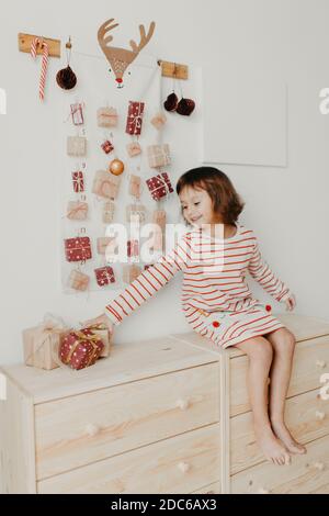 Cute girl opening Christmas Advent calendar gifts. Wrapped gifts for children. Seasonal tradition. Eco friendly Christmas Stock Photo